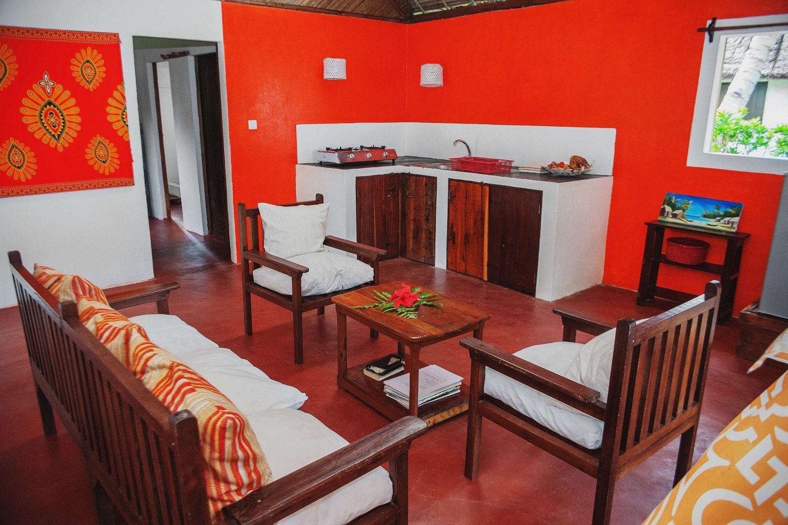 Salon d'une villa Piment Vanille : murs rouges, fauteuils en bois et fleur d'hibiscus